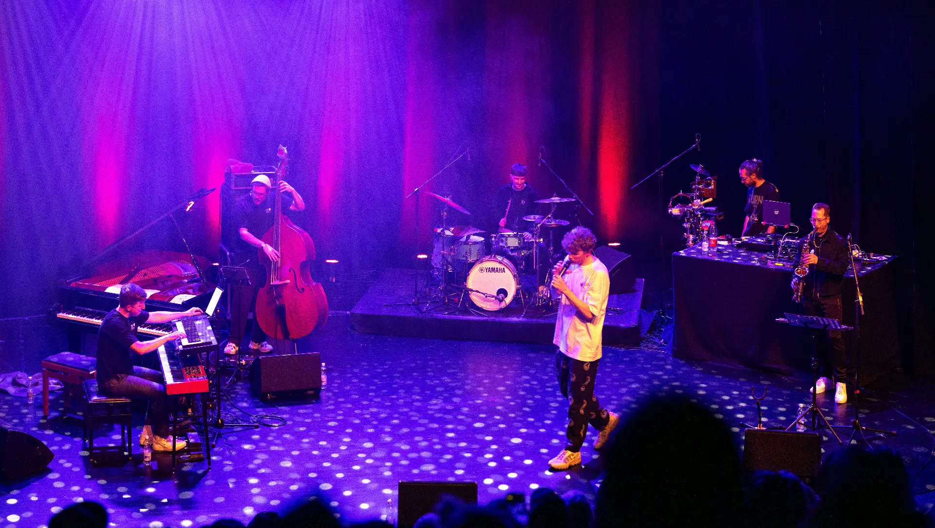 Dexter and Urban Beats Collective on stage under purple and red light, Julian Feuchter at the drums